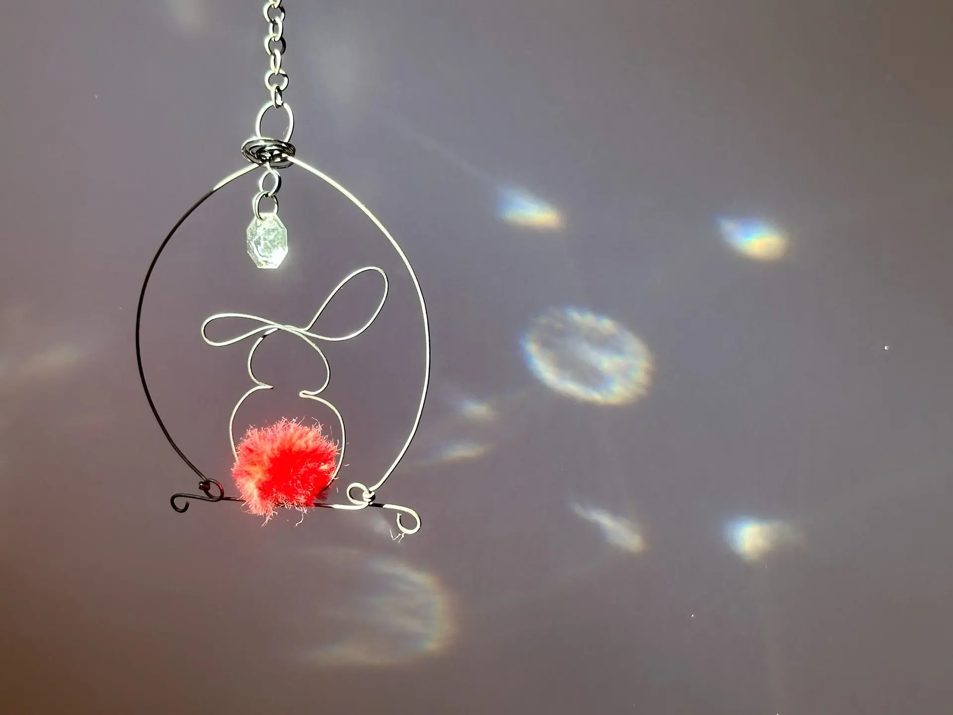 Mobile suspendu lapin en fil de fer et laine tangerine, pampille et jeu de lumière sur le mur, création Instant Flottant